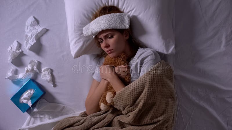 Lonely sick woman hugging teddy-bear lying in bed with compress and tissues stock photos Lonely sick woman hugging teddy-bear lying in bed with compress and tissues stock photos