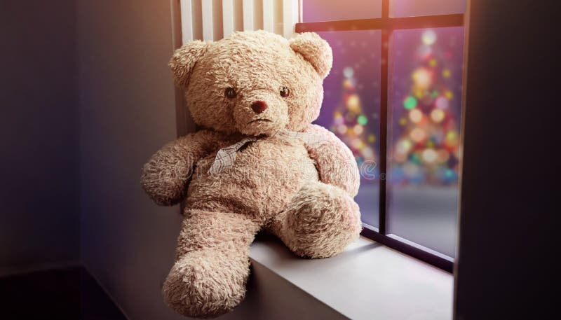 Lonely Teddy Bear Sitting nearby Window in House on Christmas Night, Xmas Tree with Lights as oute view