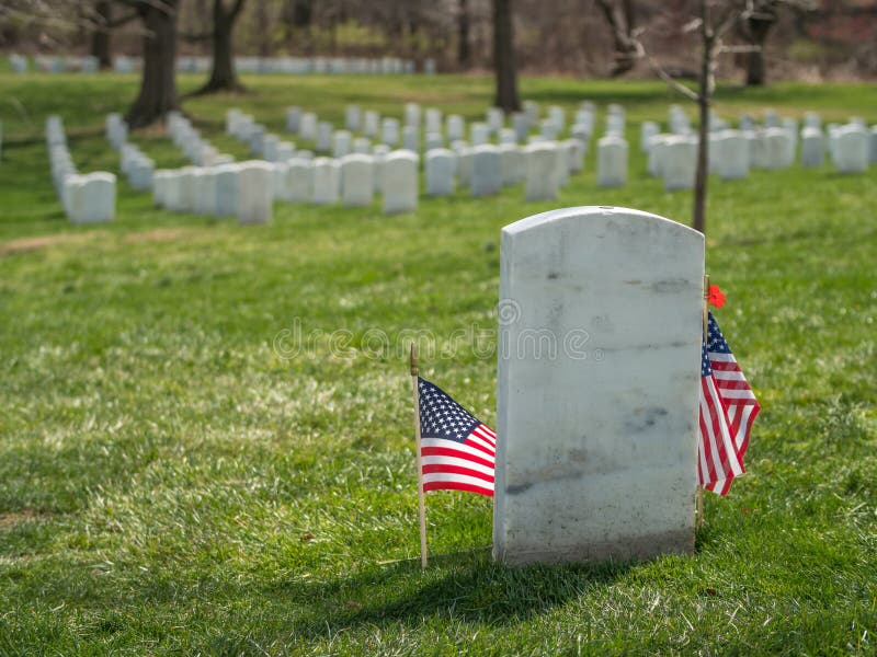 Two stars and stripes flags enframe a white gravestone at Arlington National Cemetery Virginia VA near Washington DC United States. Two stars and stripes flags enframe a white gravestone at Arlington National Cemetery Virginia VA near Washington DC United States