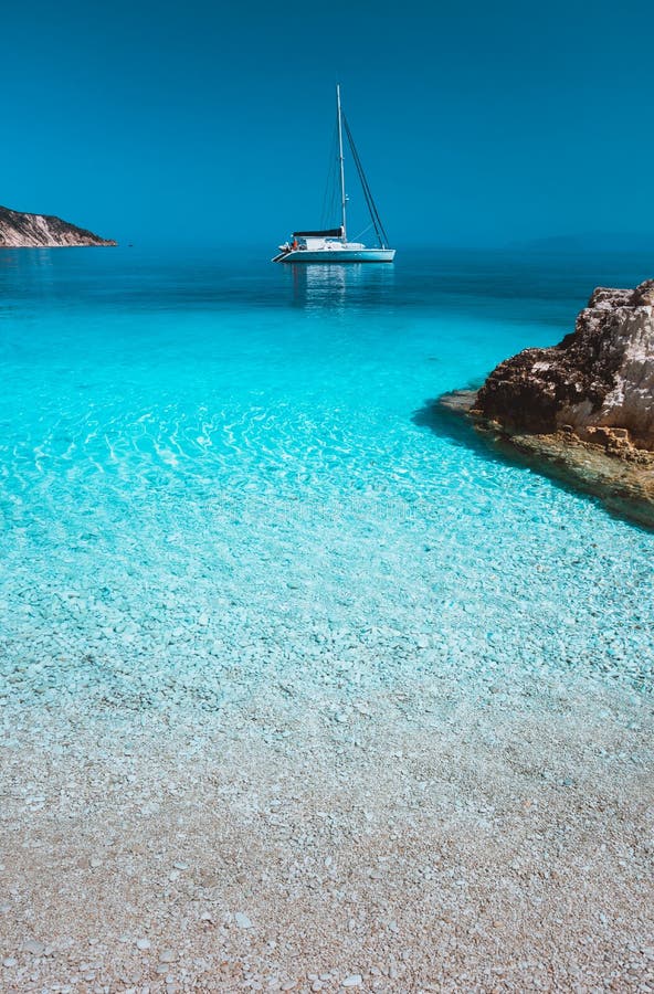 Lonely white sailing catamaran boat drift on calm sea surface. Pure azure clean blue lagoon with shallow water and