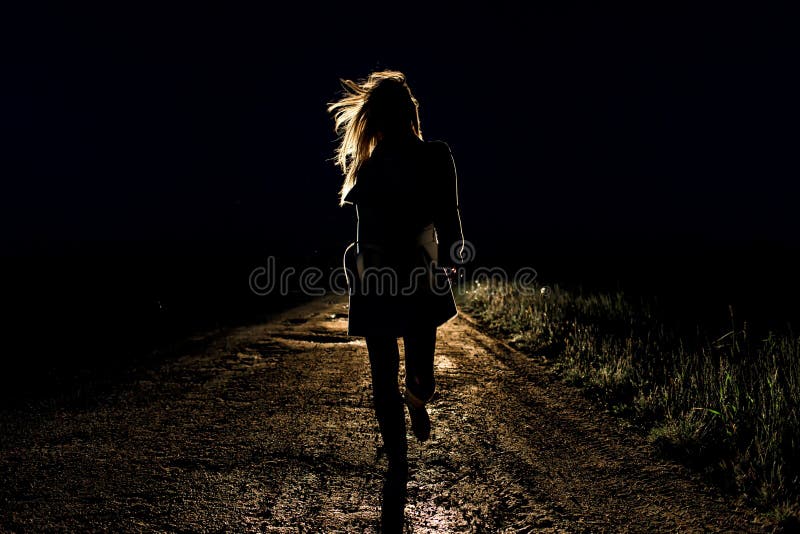 Lonely young frightened woman on an empty night road runs away in the light of the headlights of her car stock image Lonely young frightened woman on an empty night road runs away in the light of the headlights of her car stock image
