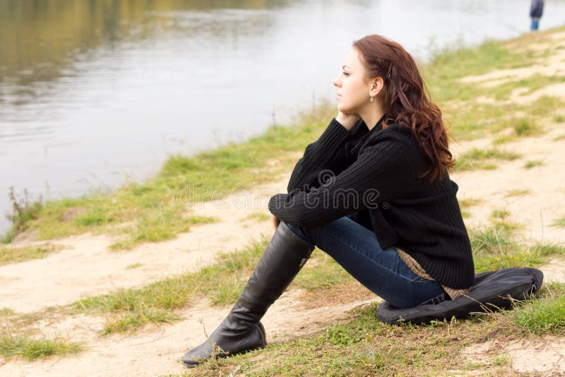 Lonely young woman sitting on a lake shore