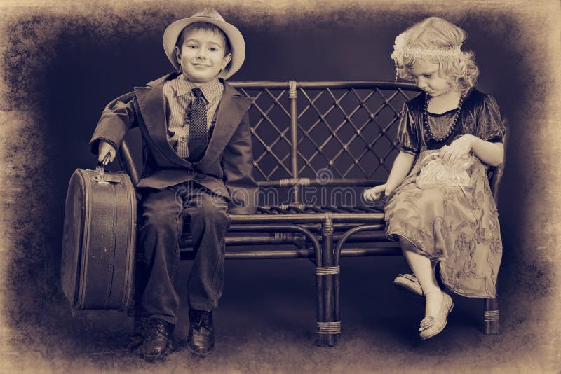 Cute little boy with an old suitcase is sitting on a bench with charming little lady. Retro style. Lovely european female stock images, royalty-free photos and pictures