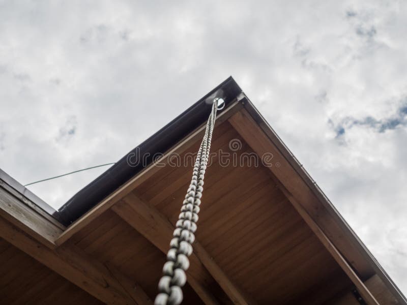 A Long Chain Hangs from the Corner of the Roof of a House Amid Clouds