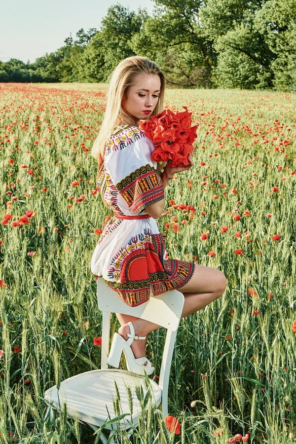 Long-haired blonde young woman in a white short dress on a field of green wheat and wild poppies stock images Long-haired blonde young woman in a white short dress on a field of green wheat and wild poppies stock images