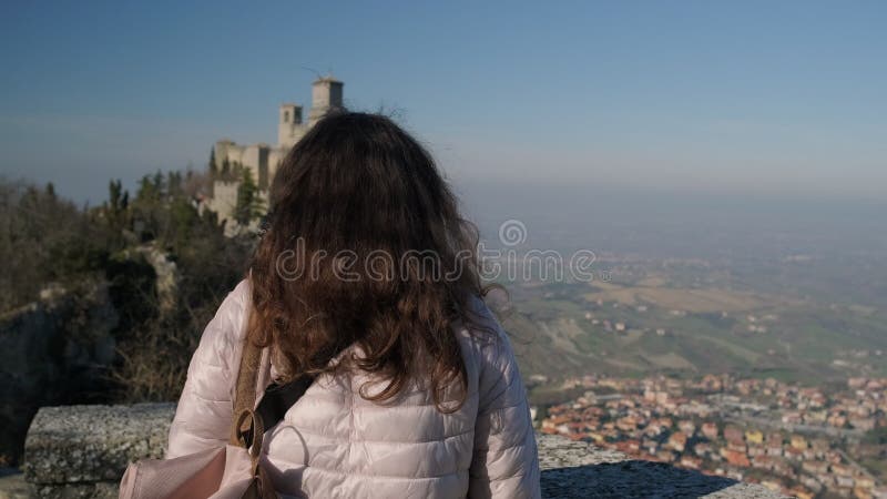 Long haired brunette admires Fortress of Guaita tower