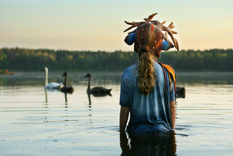 Long haired teenage girl wearing Antler bambi hat is staying waist-deep in the water watching swans family