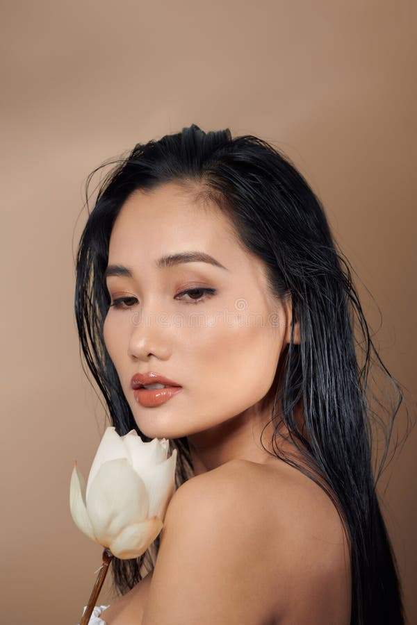 Long-haired woman in top with bare shoulders holding dried lotus buds on beige background.