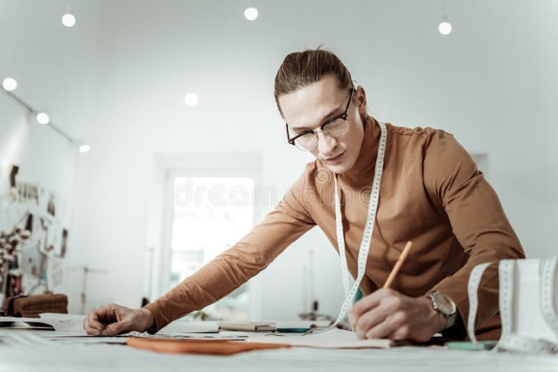 Long-haired young designer from a fashion school in a brown garment making notes