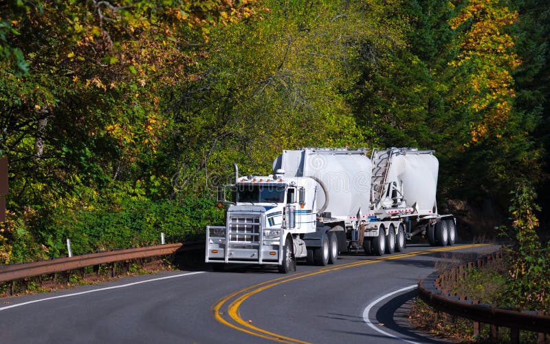 Long haul Semi Truck bulk trailers on autumn winding road