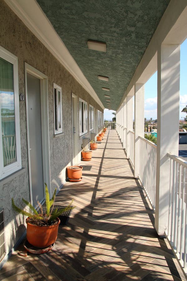 Long Motel outdoors veranda with vanishing point perspective. Potted plants and sunshine and shadows of the railings. Modern and clean stock photography Long Motel outdoors veranda with vanishing point perspective. Potted plants and sunshine and shadows of the railings. Modern and clean stock photography