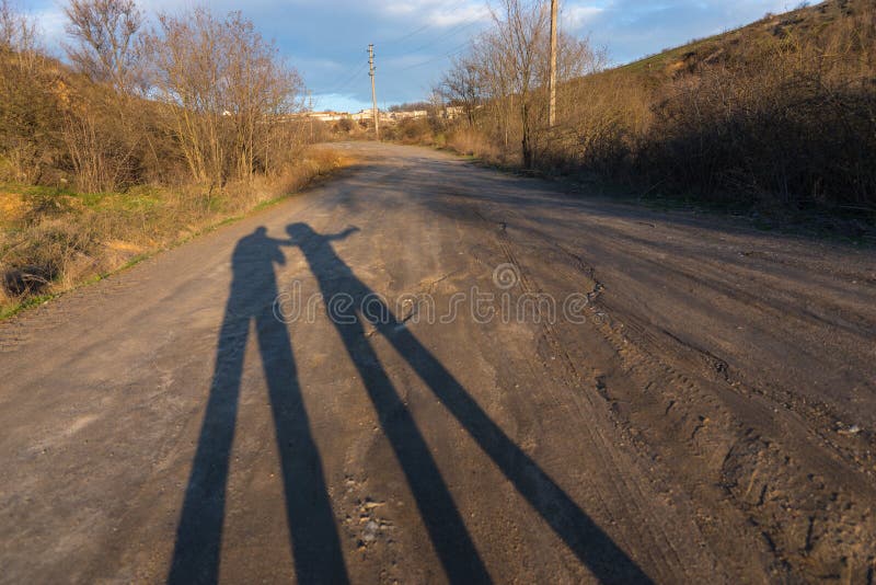 Long Shadows of Couple on Dirt Road at Sunset