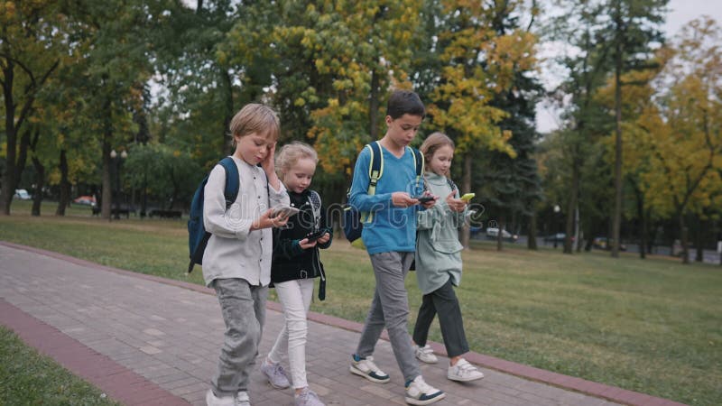 Long shot of four pupils with backpacks going out of school and talking. children use smartphones while walking from