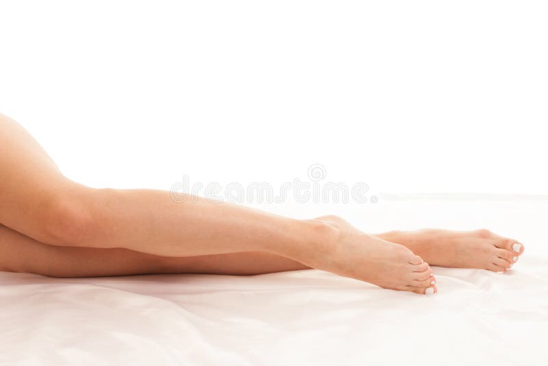 Long and slim woman legs on white sheets in bed isolated over white background stock photo Long and slim woman legs on white sheets in bed isolated over white background stock photo