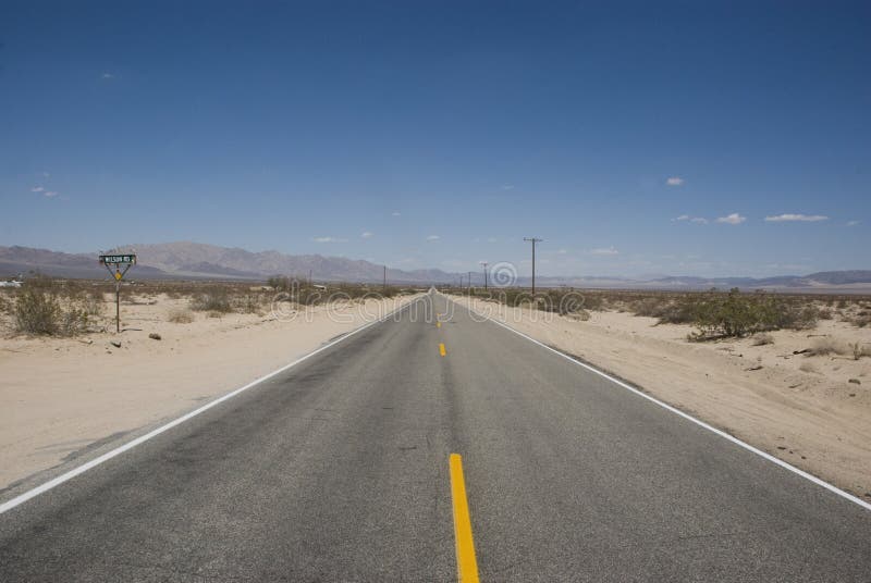 Long straight road through barren desert landscape of California