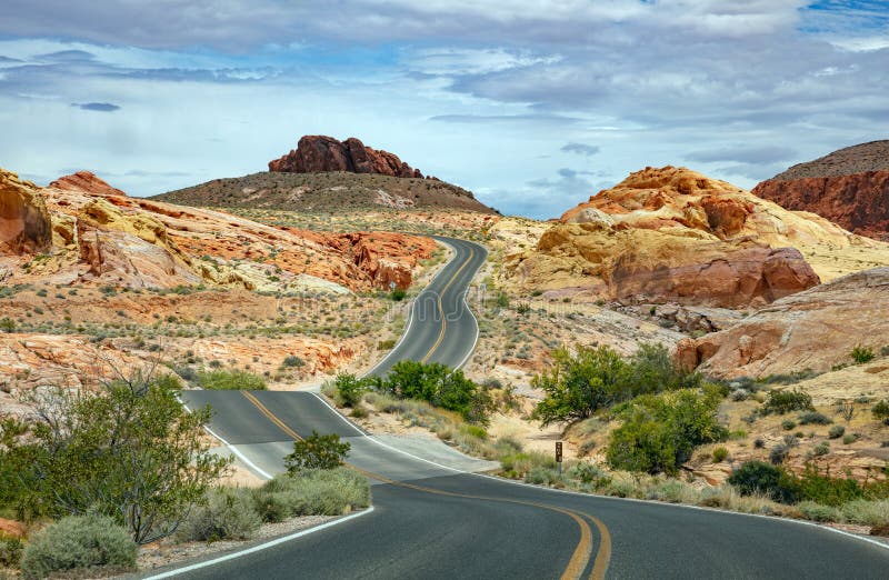 Long winding highway with ups and downs, cloudy blue sky. Valley of Fire Nevada, USA