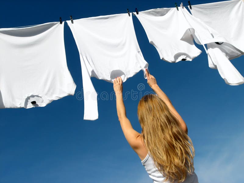 Dlouhosrstý mladá žena dosažení bílého prádla, které visí na čištění v letní vánek na oblečení-line.