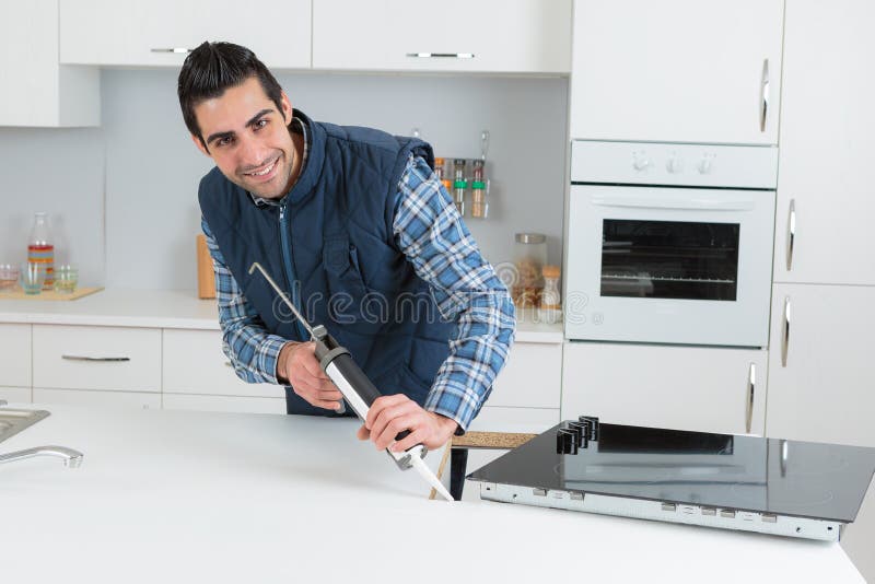 Loodgieter die siliconedichtingsproduct in keuken zetten royalty-vrije stock foto's Loodgieter die siliconedichtingsproduct in keuken zetten royalty-vrije stock foto's