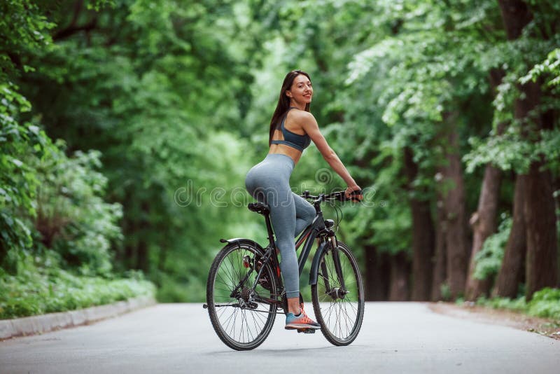 Looking behind. Female cyclist on a bike on asphalt road in the forest at daytime stock photos Looking behind. Female cyclist on a bike on asphalt road in the forest at daytime stock photos