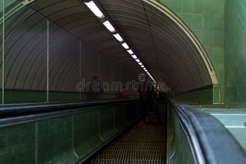 Looking down through a dark inclined escalator tunnel in subway undergraound setting with cyclists carrying bikes royalty free stock image Looking down through a dark inclined escalator tunnel in subway undergraound setting with cyclists carrying bikes royalty free stock image