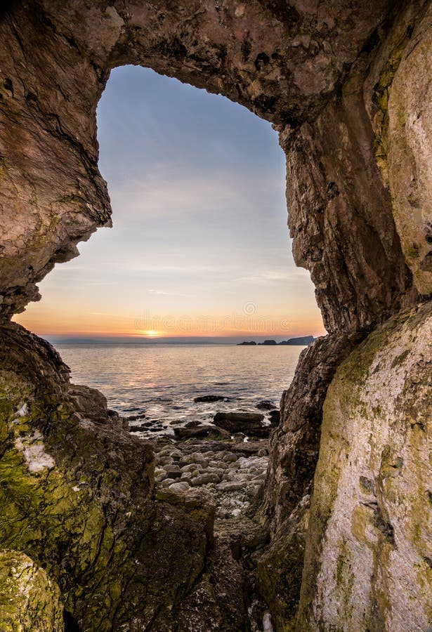 Looking out of a limestone cave to the rising sun on the horizon. Carrick-a-Rede