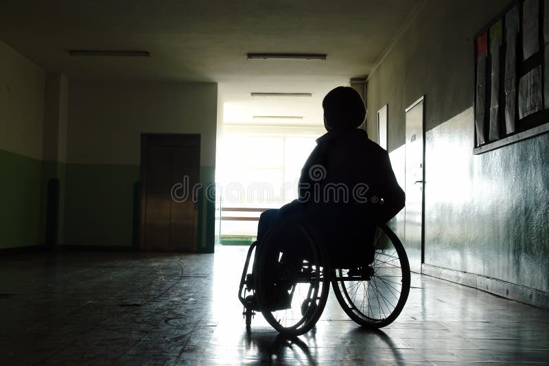 Silhouette dei portatori di donna seduta su una sedia a rotelle in ospedale corridoio, guardando verso la luce proveniente ciaspolade finestra.