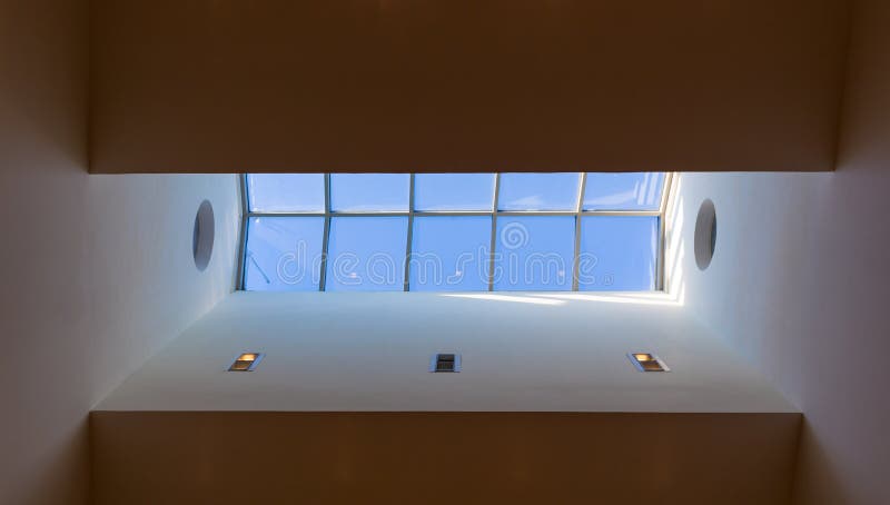 Looking up to the blue cloudy sky through modern square ceiling window