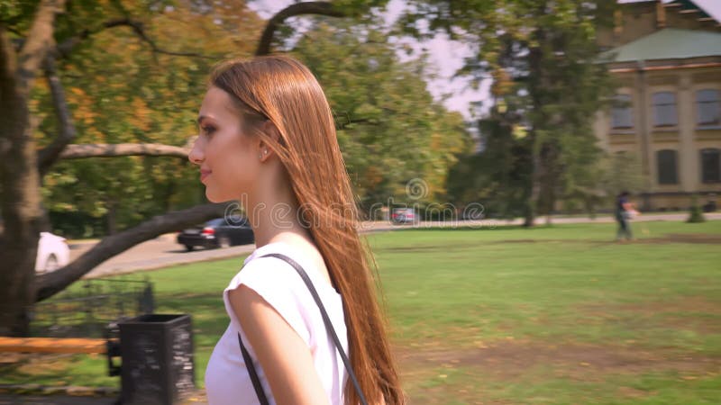 Loopt de jonge vrouw van Nice in park in dag in de zomer, horloge rond, voortbouwend op achtergrond