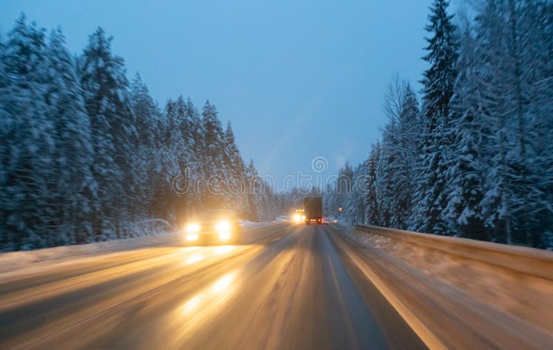 Cars Drive with Headlights on the Winter Road in a Snow Storm in the