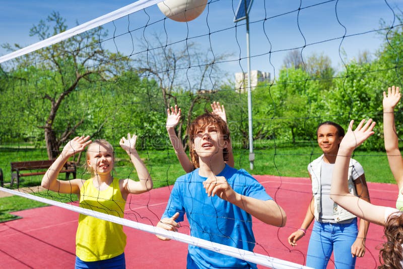 Teenagers are playing volleyball near the net on the court during sunny summer day outside. Teenagers are playing volleyball near the net on the court during sunny summer day outside