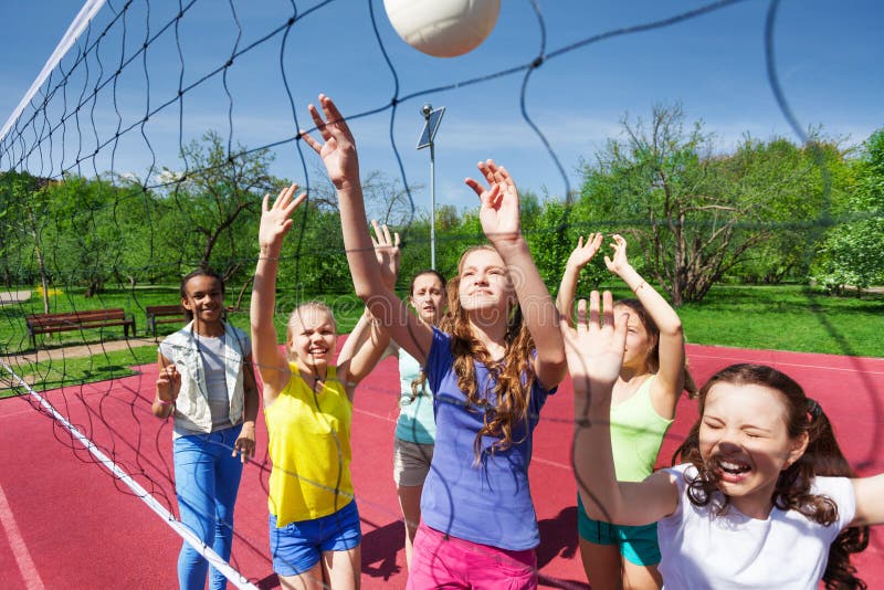 Sportive teenagers are playing volleyball near the net on the court during sunny summer day outside. Sportive teenagers are playing volleyball near the net on the court during sunny summer day outside