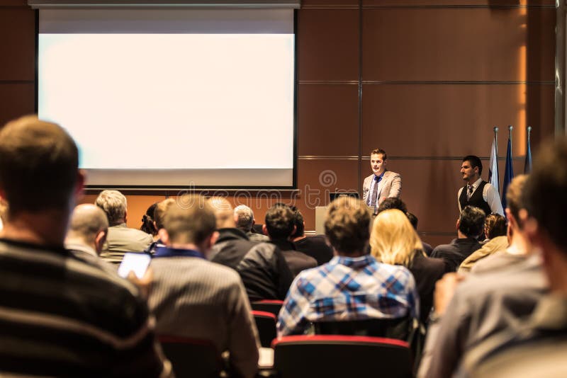 Speaker giving a talk in conference hall at business meeting event. Rear view of unrecognizable people in audience at the conference hall. Business and entrepreneurship concept. Speaker giving a talk in conference hall at business meeting event. Rear view of unrecognizable people in audience at the conference hall. Business and entrepreneurship concept.