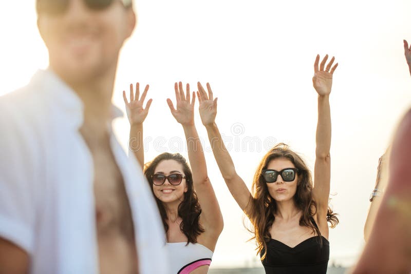 Los amigos bailan en la playa bajo luz del sol de la puesta del sol, divirtiéndose, feliz, gozan imagenes de archivo Los amigos bailan en la playa bajo luz del sol de la puesta del sol, divirtiéndose, feliz, gozan imagenes de archivo