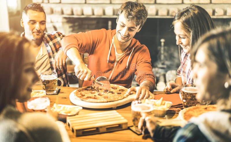 Los amigos felices agrupan la consumición de la pizza en el restaurante de la barra del chalet imagen de archivo libre de regalías Los amigos felices agrupan la consumición de la pizza en el restaurante de la barra del chalet imagen de archivo libre de regalías