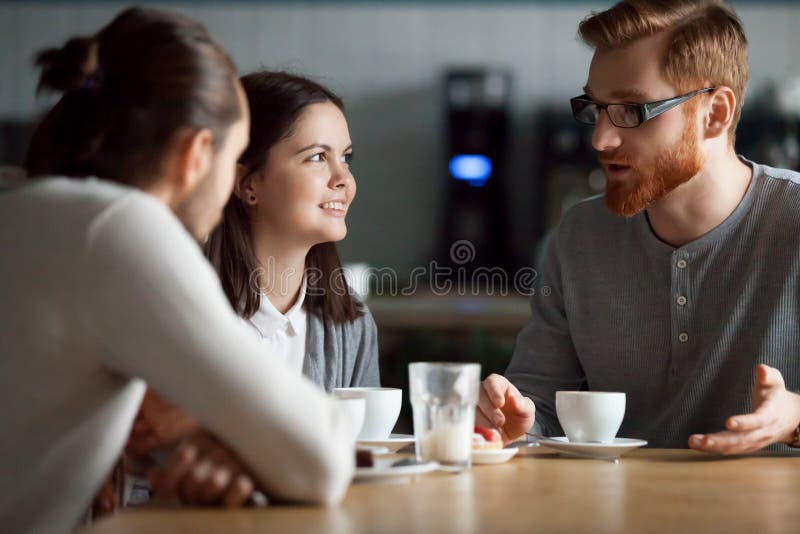 Los amigos felices hablan comiendo el café que cuelga juntos en café