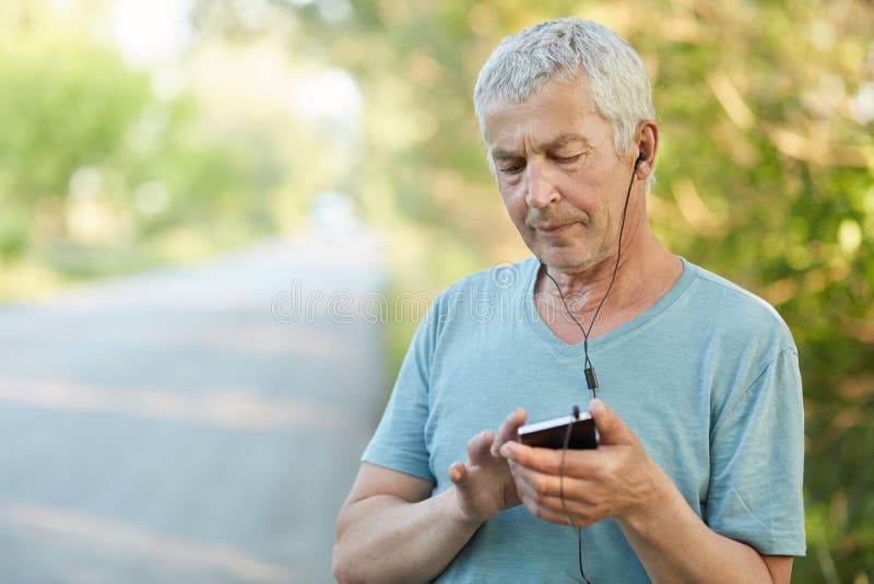 Los ancianos serios arrugaron las aplicaciones masculinas teléfono elegante y los auriculares para la música que escucha, enfocad fotos de archivo Los ancianos serios arrugaron las aplicaciones masculinas teléfono elegante y los auriculares para la música que escucha, enfocad fotos de archivo