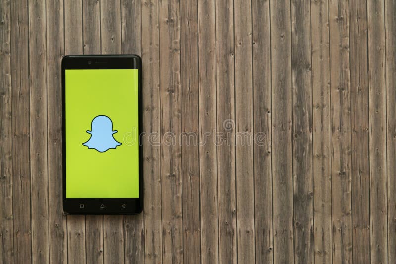 Snapchat logo on smartphone screen on wooden background.