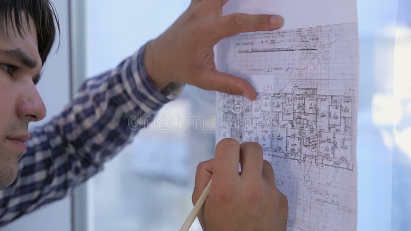 Los arquitectos irreconocibles dan el trabajo con el bosquejo, dibujo, planean cerca de ventana panorámica de la oficina limpia b