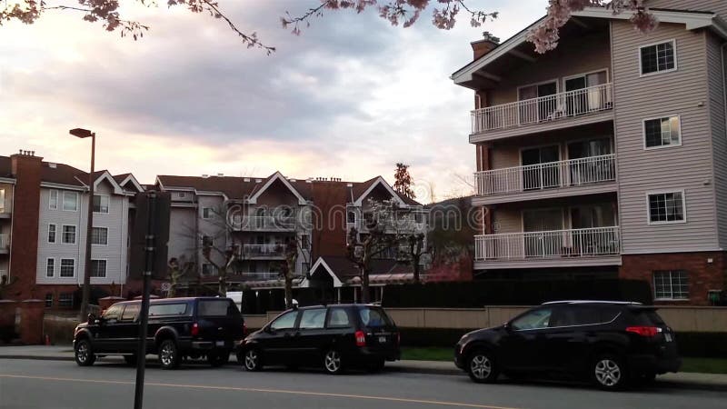 Los coches montan por la calle con el edificio en el tiempo de primavera