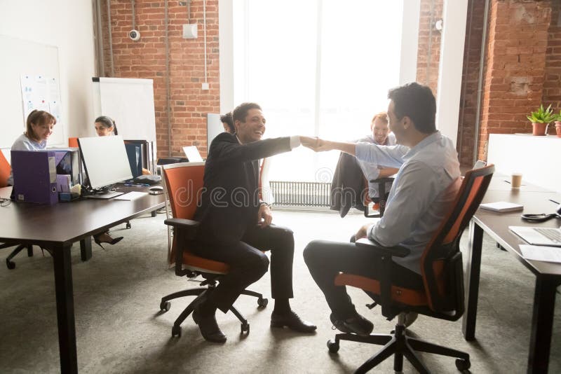 Los colegas masculinos emocionados dan los puños topan en oficina imagen de archivo Los colegas masculinos emocionados dan los puños topan en oficina imagen de archivo