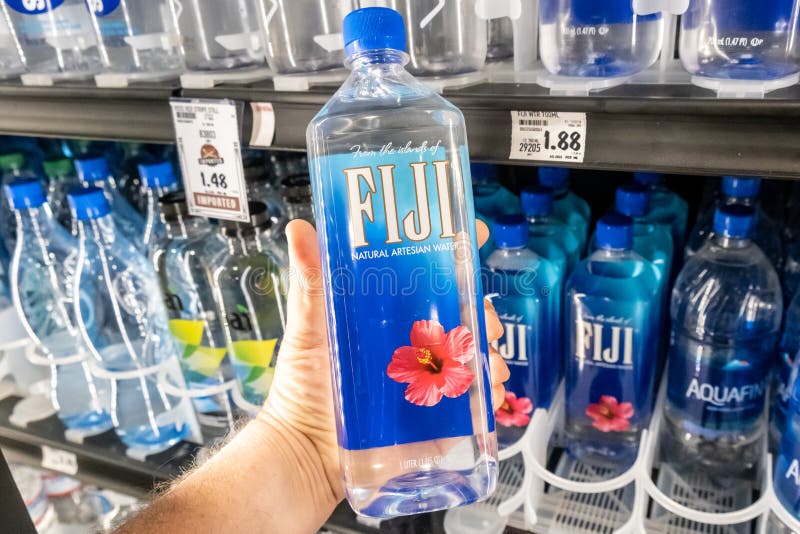 Los compradores dan sostener una botella plástica de agua artesiana natural de la marca de Fiji fotos de archivo libres de regalías Los compradores dan sostener una botella plástica de agua artesiana natural de la marca de Fiji fotos de archivo libres de regalías