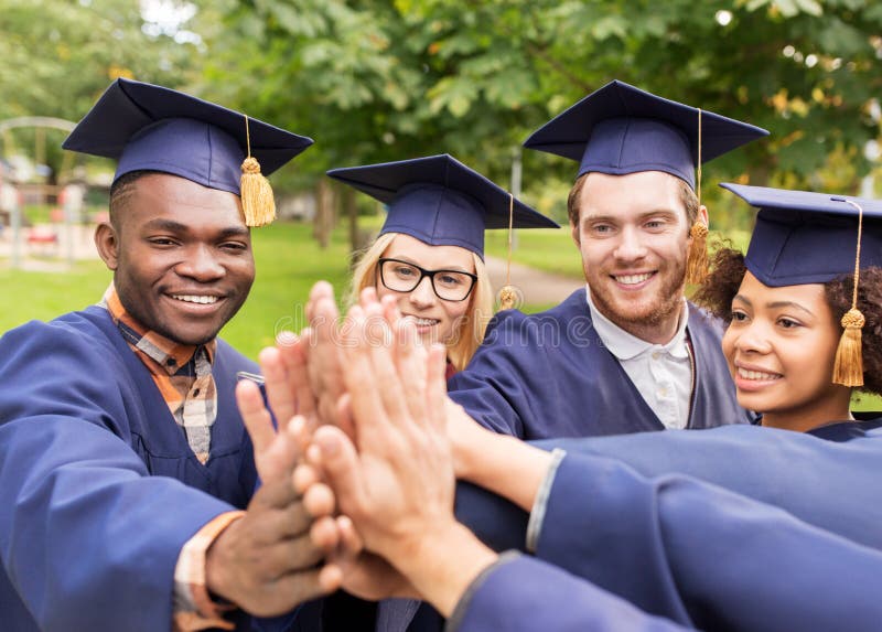 Los estudiantes felices en mortero suben a hacer el alto cinco. Educación, graduación y concepto de la gente - el grupo de estudiantes internacionales felices en tableros y soltero del mortero viste la fabricación del alto cinco