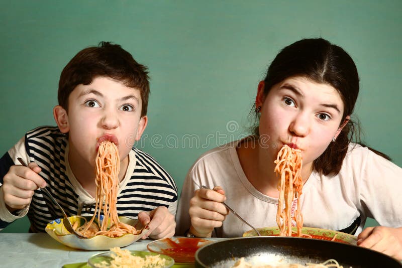 Los hermanos adolescentes felices muchacho y muchacha comen los espaguetis imagen de archivo libre de regalías Los hermanos adolescentes felices muchacho y muchacha comen los espaguetis imagen de archivo libre de regalías