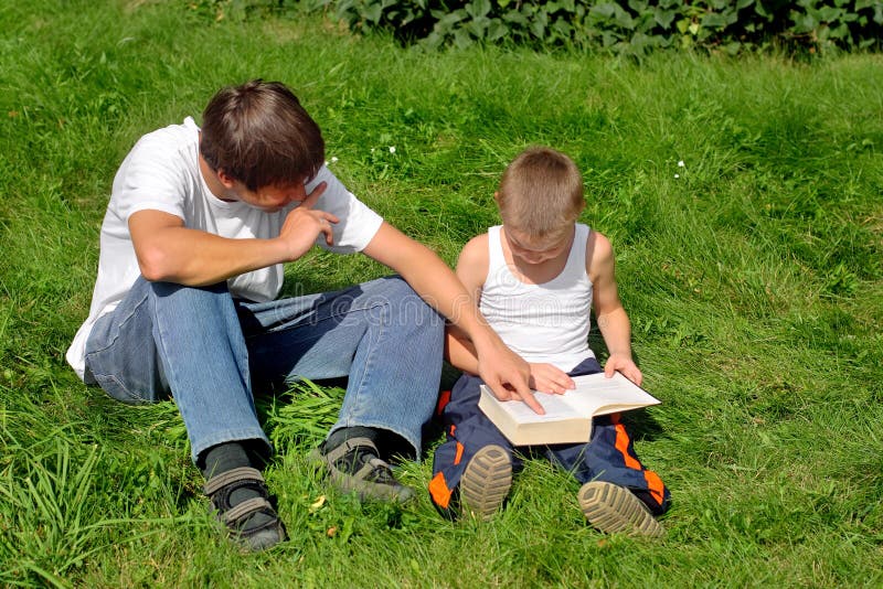 Little and Older Brothers reads a book in the Summer Park. Little and Older Brothers reads a book in the Summer Park