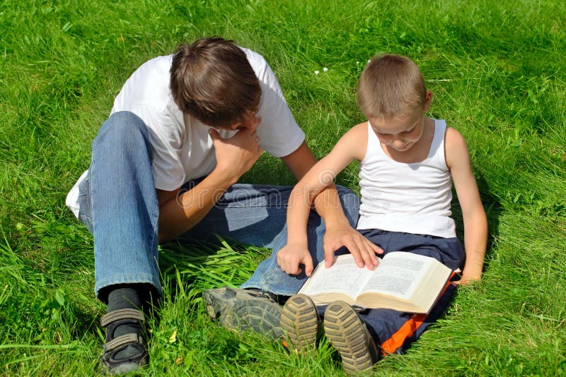 Little and Older Brothers reads a book in the Summer Park. Little and Older Brothers reads a book in the Summer Park