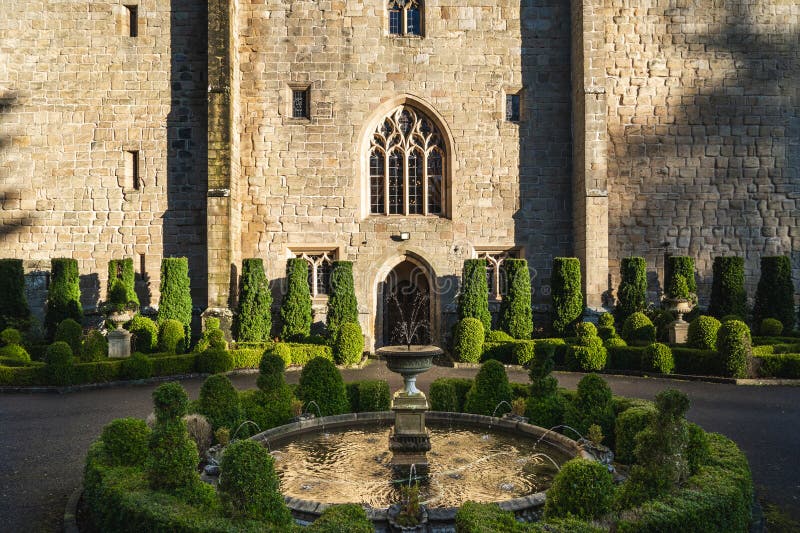 The formal garden and front doorway of a historic castle with ornate fountain and neatly trimmed topiary trees. The formal garden and front doorway of a historic castle with ornate fountain and neatly trimmed topiary trees