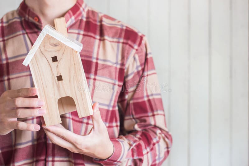Los hombres jovenes llevan la camisa roja de la guinga que lleva a cabo el modelo miniatura de la casa en el fondo de madera blan imagenes de archivo Los hombres jovenes llevan la camisa roja de la guinga que lleva a cabo el modelo miniatura de la casa en el fondo de madera blan imagenes de archivo
