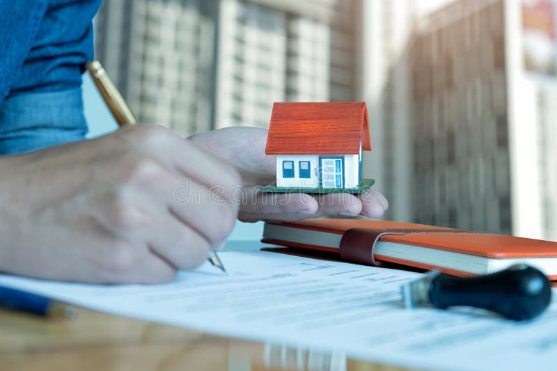 Los hombres tienen una casa modelo a mano, la otra mano están utilizando una firma de la pluma imagen de archivo Los hombres tienen una casa modelo a mano, la otra mano están utilizando una firma de la pluma imagen de archivo