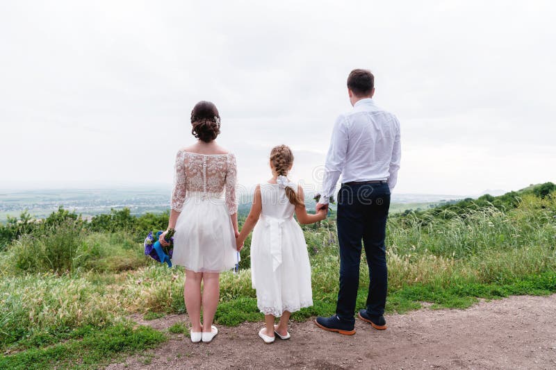 Los jóvenes casados se juntan y su pequeña hija el día de boda se está colocando en la naturaleza que lleva a cabo las manos imagenes de archivo