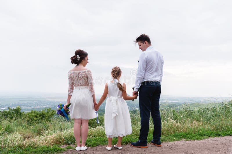 Los jóvenes casados se juntan y su pequeña hija el día de boda se está colocando en la naturaleza que lleva a cabo las manos foto de archivo